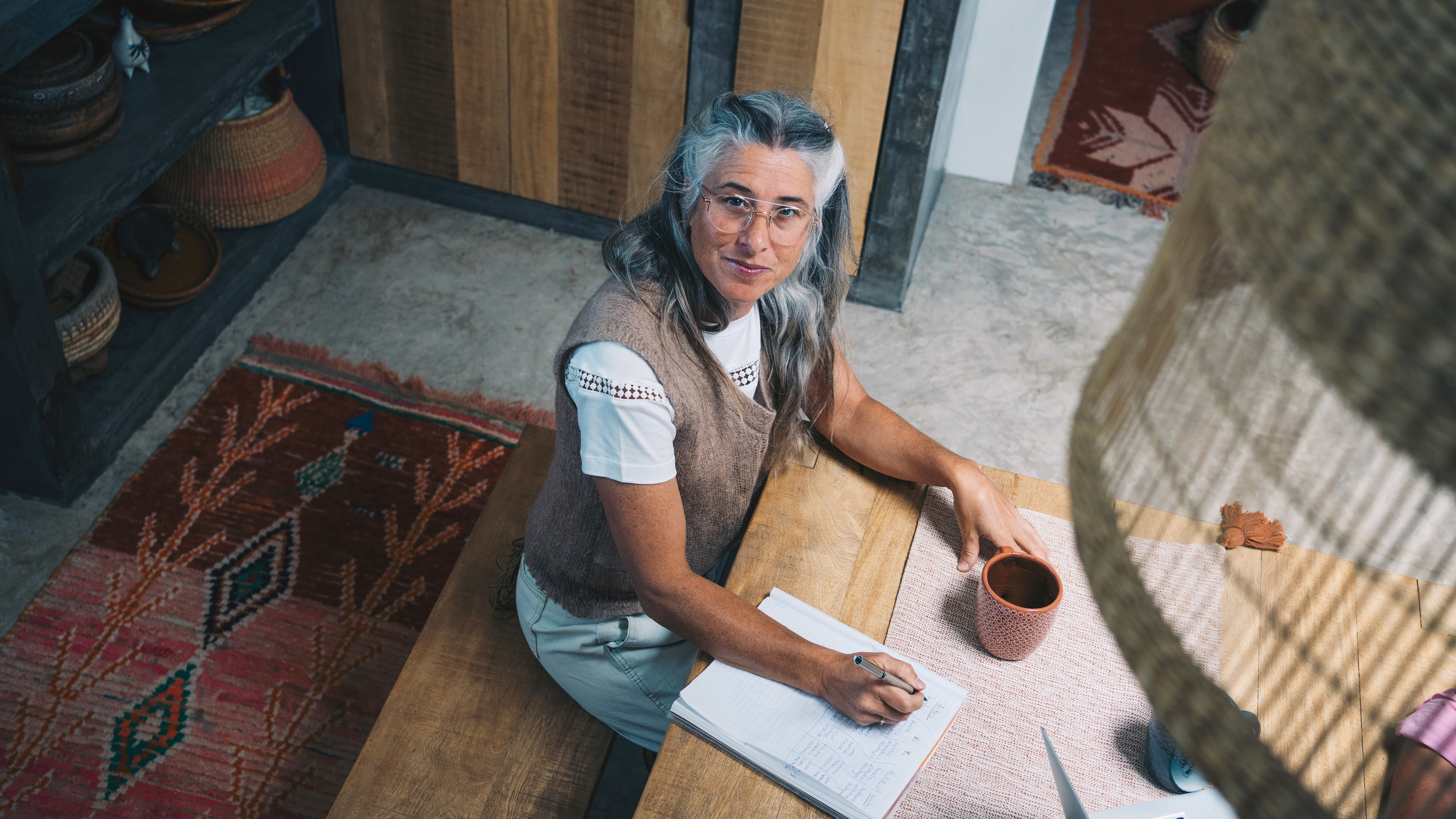 Geneviève Vena assise à une table, un stylo à la main devant son carnet